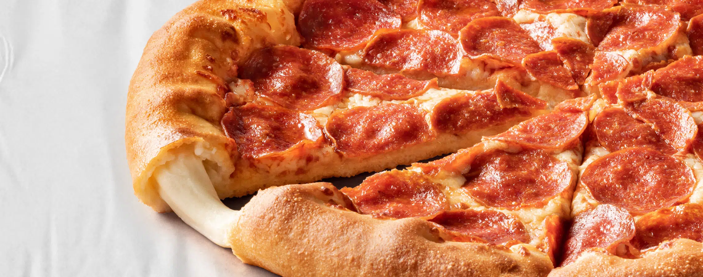 Pizza with pepperoni slices cheese-stuffed crust and melty cheese displayed on a white surface.