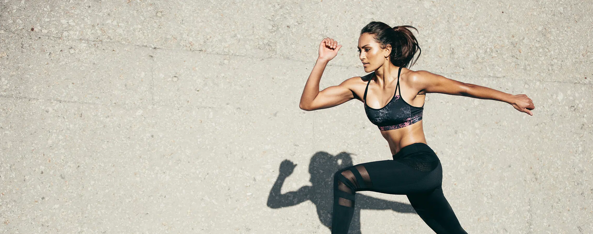 A woman runs energetically against a textured concrete wall.