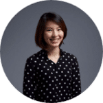 A person smiles while standing against a plain gray background wearing a black shirt with white polka dots.