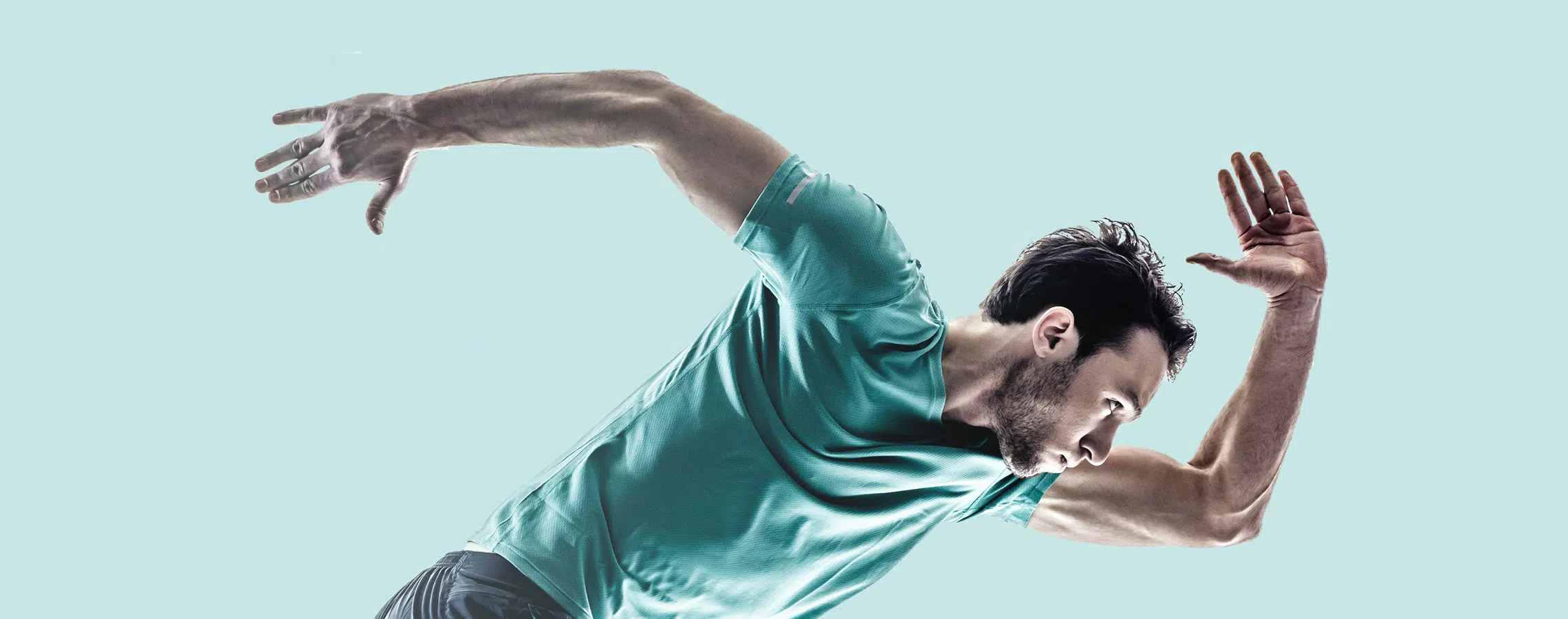 Man in a teal shirt sprinting arms back against a light blue background.