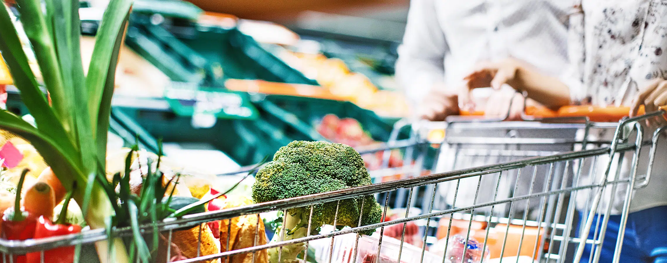 Grocery cart filled with fresh vegetables like broccoli and peppers in a supermarkets produce section.