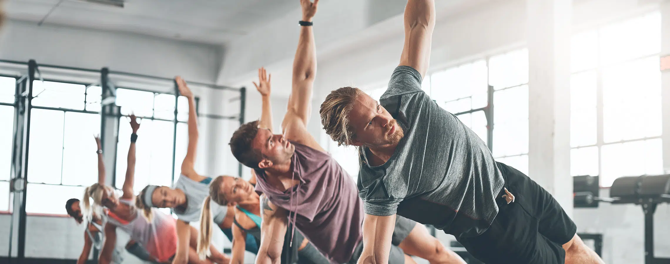 People doing side plank exercises in a bright gym with large windows.