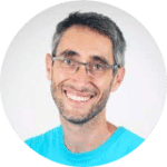 A person smiling wearing glasses and a blue shirt set against a plain white background.