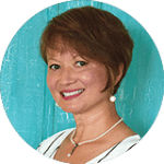 A person smiles against a textured teal background wearing a striped outfit pearl earrings and necklace.