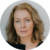 A person with wavy hair is looking forward against a plain light-colored background.