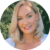 A person smiling softly set against a leafy green background.