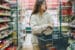 A woman holding a shopping basket walks through a supermarket aisle filled with various packaged foods.