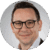 A person wearing glasses smiles at the camera. The background is a plain light gray gradient.