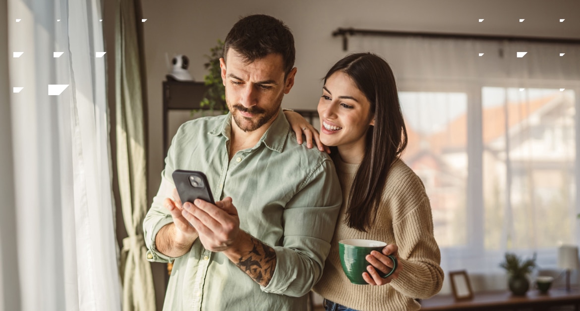 Young heterosexual couple in their 20s-30s looking at a phone together in their home.
