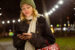 Young Woman walking outside in winter, holding a phone surrounded by holiday lights