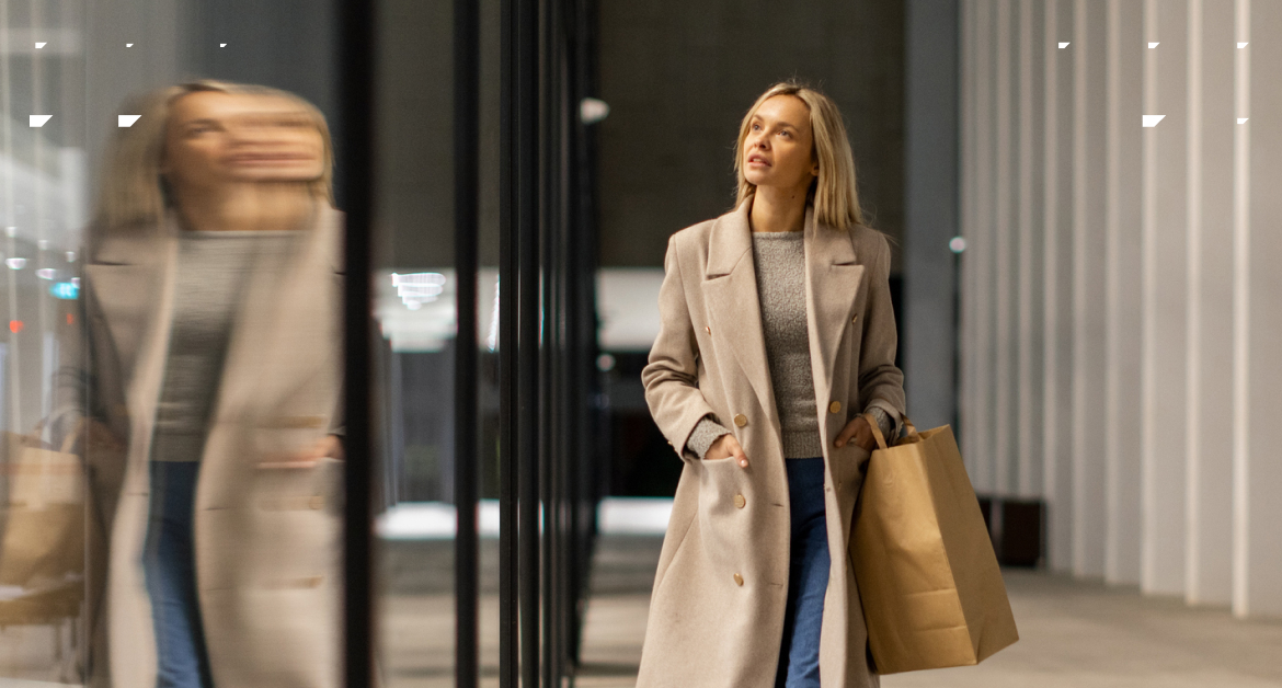 Female shopper in her 20s/30s walking in a mall in a winter coat.