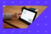 Marketer tapping a tablet screen on a desk showing a marketing automation workflow.