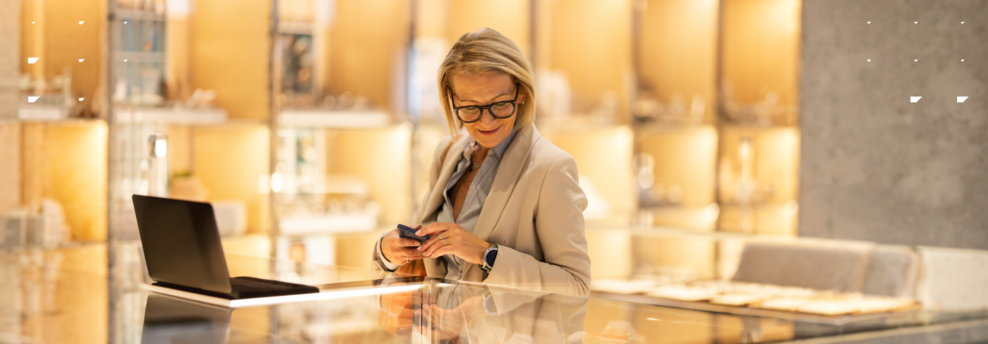 Woman in her 50s in a premium retail environment looking at a laptop while holding her phone.