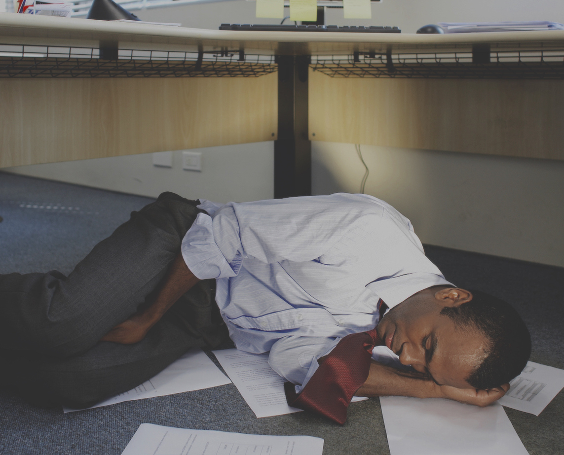 adult-man-sleeping-under-desk-papers-on-floor